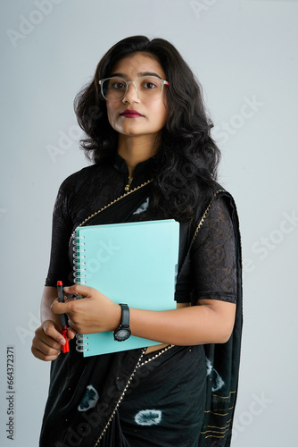 Portrait of Indian lady teacher in saree stands against white or blackboard , conducting online class using Camera, internet and lights