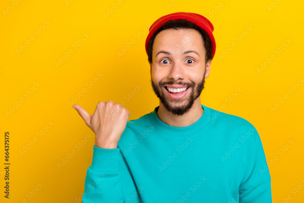 Photo of impressed ecstatic man wear red beanie hat teal sweater indicating at offer empty space isolated on yellow color background Photo of impressed ecstatic man wear red beanie hat teal sweater indicating at offer empty space isolated on yellow color background
