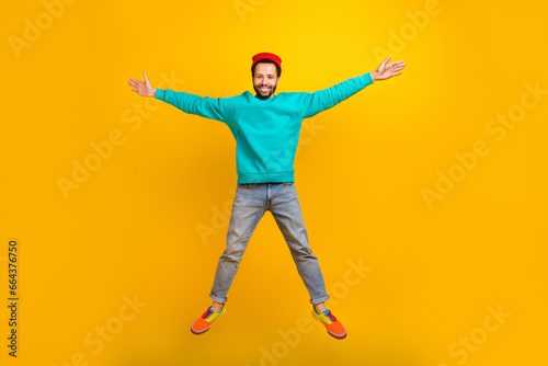 Full size photo of satisfied optimistic guy dressed red hat denim trousers flying in star pose isolated on yellow color background