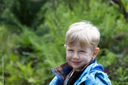 Portrait of a blond boy against a background of green foliage in the park copy space