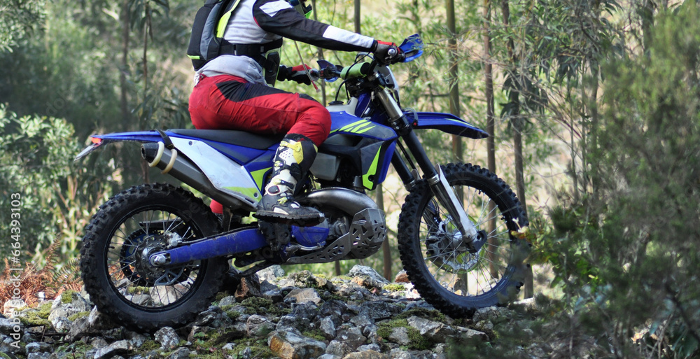 Person on a motorbike doing a mountain trail in extreme action going over a pile of rocks, off-road motorcycling hobby