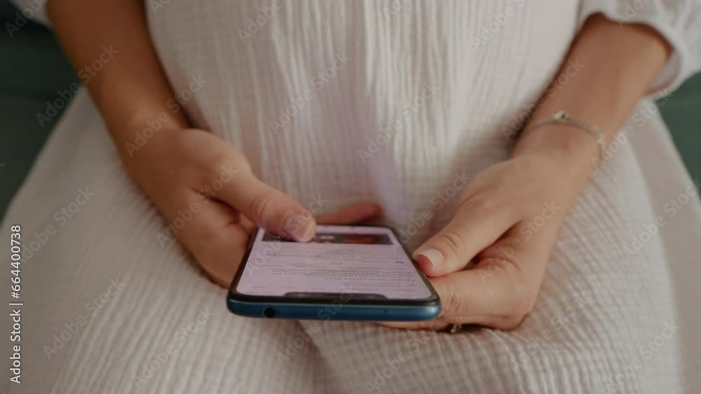 Pregnant woman sitting on the couch scrolling a mobile phone enjoy her motherhood moment. Unrecognized pregnant female with smartphone. Pregnant woman sitting on the couch scrolling a mobile phone enjoy her motherhood moment. Unrecognized pregnant female with smartphone.