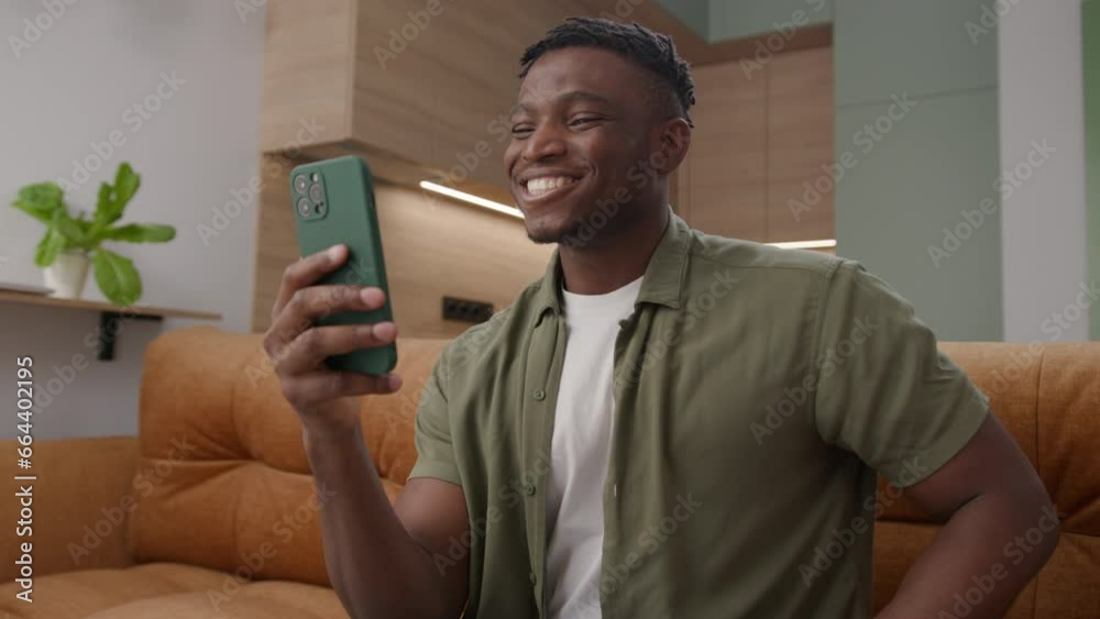 Black Man is on Video Call Using Smartphone. African American man talking to cellphone sitting on couch at home. Black Man is on Video Call Using Smartphone. African American man talking to cellphone sitting on couch at home.