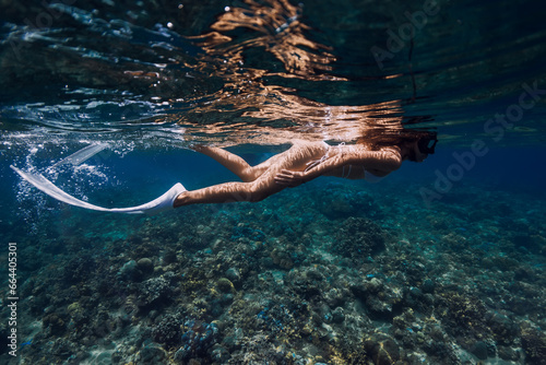 Underwater view of woman swimming near corals in transparent ocean