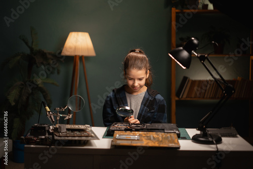 Caucasian teenage girl for searching way of fixing broken laptop. Cute child sitting at table and trying to repair laptop computer at home.