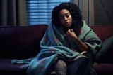 sick african american girl wrapped in blanket with cold or flu symptoms rests on sofa