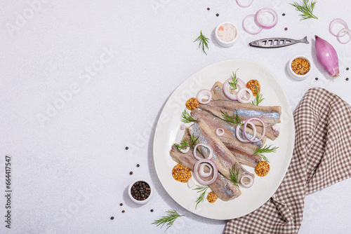 Salted herring with dijon mustard, dill and red onion rings on white stone background