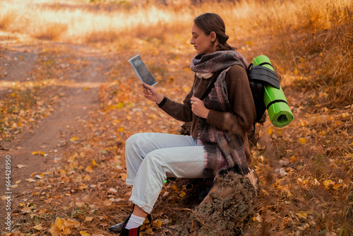 girl with a backpack and a map in the forest, sitting on a log, looking at a map in the autumn forest, autumn holidays and hiking, lifestyle concept