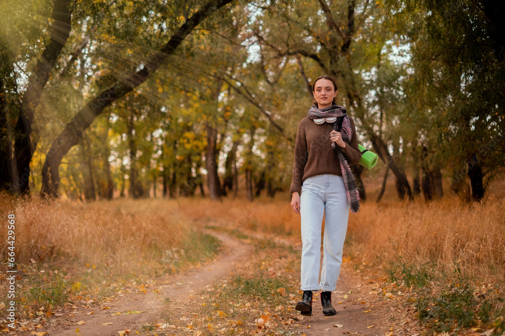 Fototapeta premium woman walking in the forest, female traveler walking through the forest on a sunny autumn day, young Caucasian woman hiking, girl with a tourist backpack walking in the forest