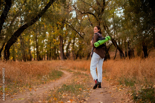 woman walking in the forest, female traveler walking through the forest on a sunny autumn day, young Caucasian woman hiking, girl with a tourist backpack walking in the forest