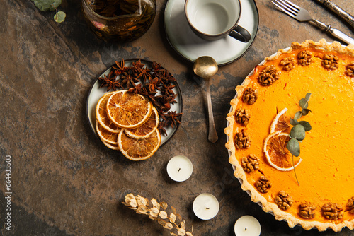 thanksgiving theme, garnished pumpkin pie near candles and orange slices with spices on stone table