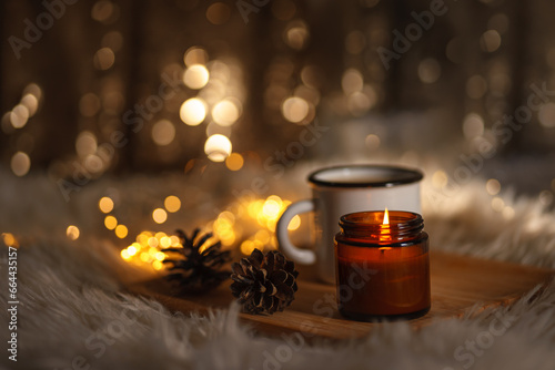 christmas still life with candle. new year christmas card. lights of garlands, lighted candle and a cup of coffee. comfort and hygge. selective focus. bokeh