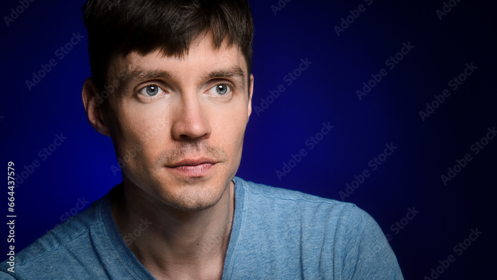 Studio portrait of Caucasian man on dark blue background. Young guy looks away. Copy space. Handsome thin guy in casual clothes. Studio portrait of Caucasian man on dark blue background. Young guy looks away. Copy space. Handsome thin guy in casual clothes.