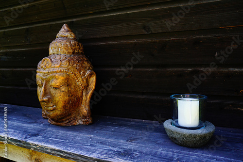 Buddhakopf auf einem Tisch und rechts davon eine weiße Kerze im ländlichen Stil. photo