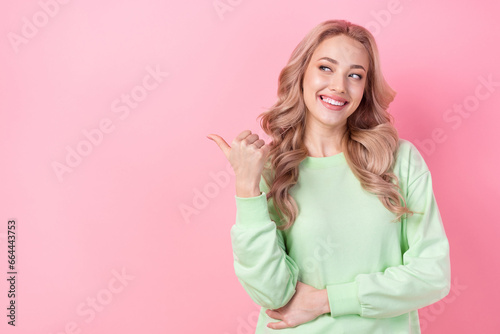 Photo of young model blonde curls wearing green jumper directing finger empty space announce event party isolated on pink color background
