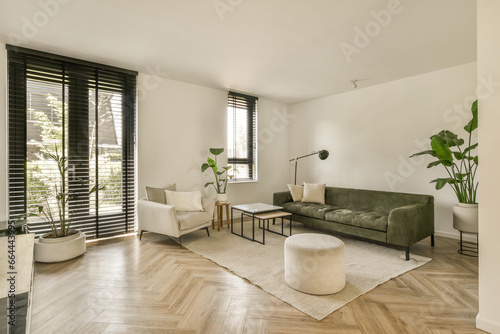 a living room with wood flooring and black shutters on the sliding glass door that leads to an outside patio