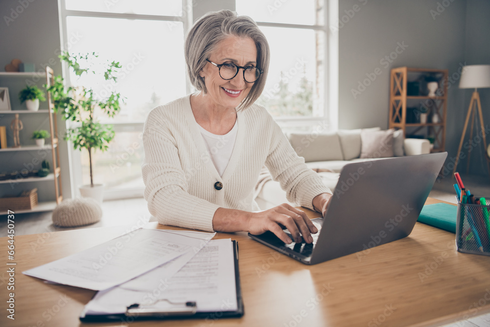 Photo of shiny adorable elderly lady entrepreneur wear white cardigan communicating modern device indoors apartment room Photo of shiny adorable elderly lady entrepreneur wear white cardigan communicating modern device indoors apartment room