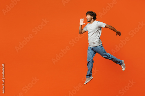 Schilderij op canvas Full body young fun Indian man he wears t-shirt casual clothes jump high run scream sharing hot news about sales discount with hands near mouth isolated on orange red color background studio portrait