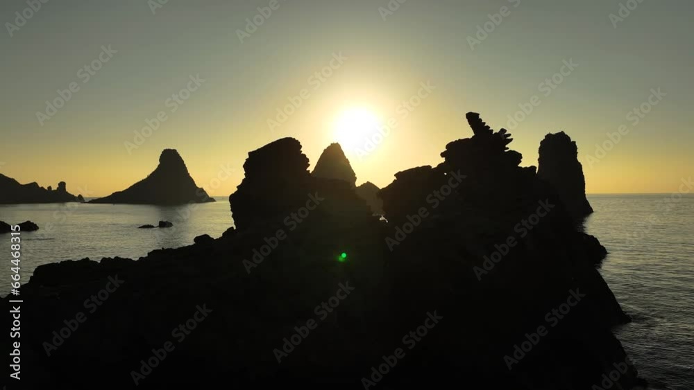 Alba sui Faraglioni dei Ciclopi, l'arcipelago di scogli difronte ad Aci Trezza, Sicilia, Italia.
Ripresa aerea controluce delle isole di Lachea con il sole giallo delle prime luci dell'alba. 
