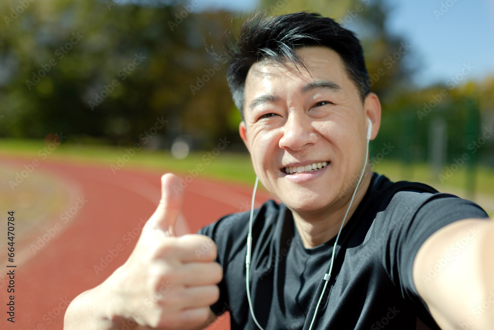 Asian young man talking in headphones on the news ringer at the stadium. Smiling and pointing at the camera with a super finger. Close-up photo. Asian young man talking in headphones on the news ringer at the stadium. Smiling and pointing at the camera with a super finger. Close-up photo.