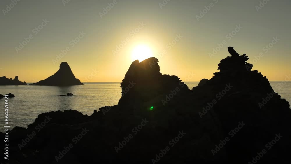 Alba sui Faraglioni dei Ciclopi, l'arcipelago di scogli difronte ad Aci Trezza, Sicilia, Italia.
Ripresa aerea controluce delle isole di Lachea con il sole giallo delle prime luci dell'alba. 