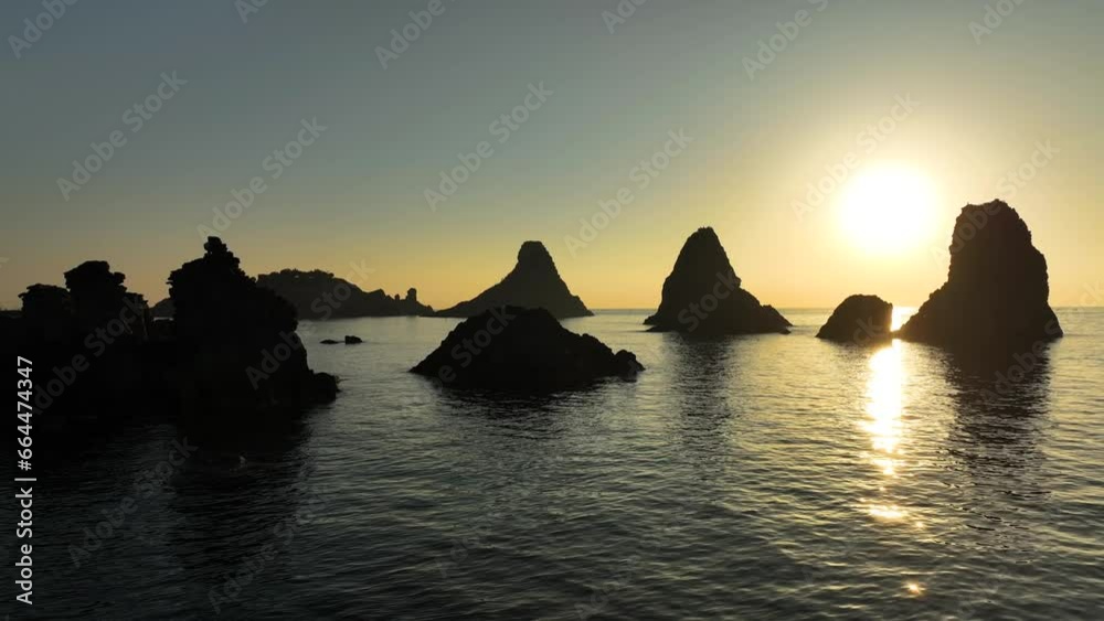 Alba sui Faraglioni dei Ciclopi, l'arcipelago di scogli difronte ad Aci Trezza, Sicilia, Italia.
Ripresa aerea controluce delle isole di Lachea con il sole giallo delle prime luci dell'alba. 