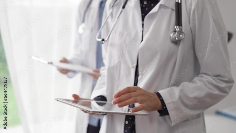 Doctor use a tablet computer for making medication notes while another physician works in the background. Medicine concept Doctor use a tablet computer for making medication notes while another physician works in the background. Medicine concept
