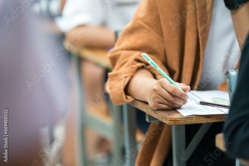 Selective focus high school or university students concentrate writing on paper answer sheet for final exam in the classroom