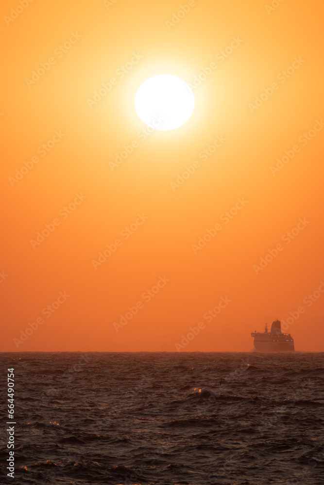 Colorful sunset on the horizon of the Aegean Sea seen from the coast of Ikaria, Greece with ferry boat in the background