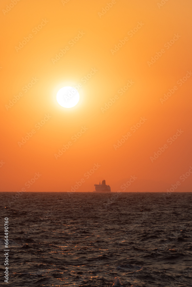 Colorful sunset on the horizon of the Aegean Sea seen from the coast of Ikaria, Greece with ferry boat in the background