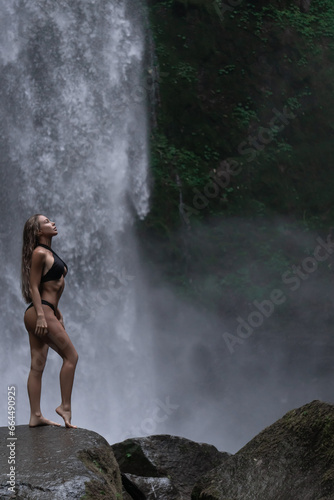 Beautiful girl in bikini posing by a waterfall