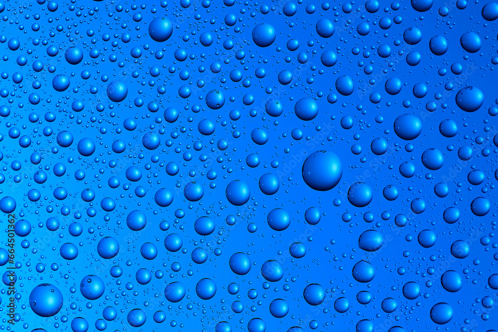Bubbles and water drops in selective focus on glass, blue background.