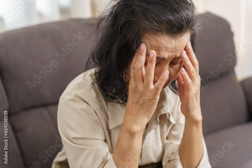 Sad middle age Asian woman touching forehead having headache suffering from migraine. mature asian woman feeling sick or depression. © Charlie's