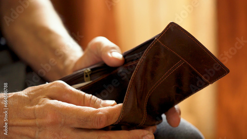 An elderly man's hands, covered with knotted veins, search for coins in his wallet