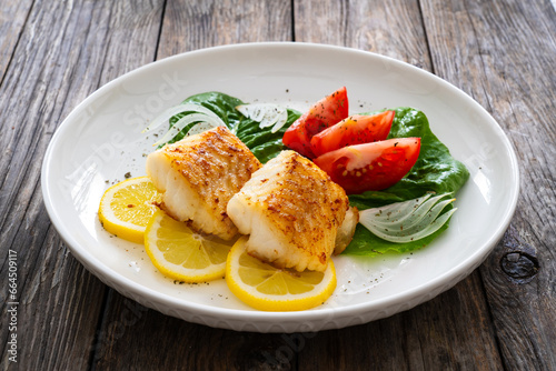 Seared cod loin and fresh vegetables on wooden table
