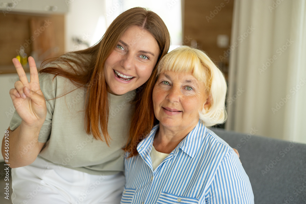 Happy senior woman enjoying in daughter's affection on Mother's day. Smiling mature mother and daughter hugging, sitting on couch at home, looking at camera. Beautiful womens say Hi. Happy senior woman enjoying in daughter's affection on Mother's day. Smiling mature mother and daughter hugging, sitting on couch at home, looking at camera. Beautiful womens say Hi.
