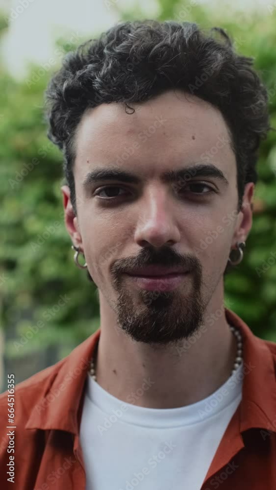 Vertical close up portrait of young man with black hair and earring looking at camera