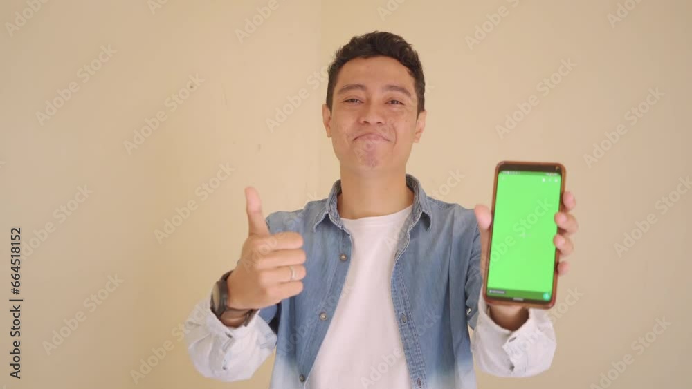 Young Indonesian man with denim style hold smartphone showing green screen. The footage is suitable to use for man expression and ecommerce content media. Young Indonesian man with denim style hold smartphone showing green screen. The footage is suitable to use for man expression and ecommerce content media.