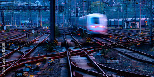 Railway panorama with leaving train in early morning twilight at blue hour. Tracks, oververhead lines, switches at Hagen main station in Ruhr basin, Germany. Transportation technology for passengers.