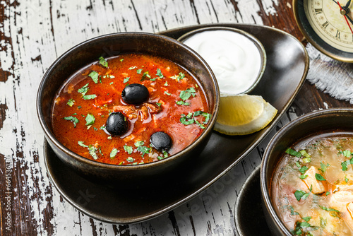 Valokuva Tasty hodgepodge soup with meat, olives, greens and sour cream on bowl on rustic wooden background