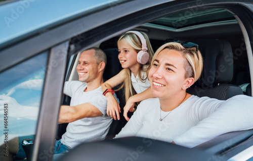 Cheerful young traditional family has a auto journey in modern car. Mother, father and daugher with headphones. Safety riding car and traveling concept image. © Soloviova Liudmyla