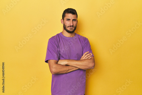 Young Hispanic man on yellow background suspicious, uncertain, examining you.