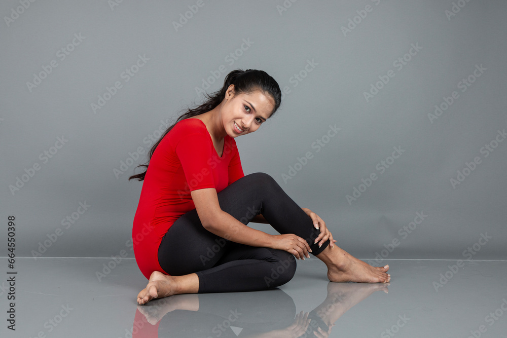 Fototapeta premium Healthy young woman in red t-shirt and black leggings doing yoga and stretching exercises isolated on grey background