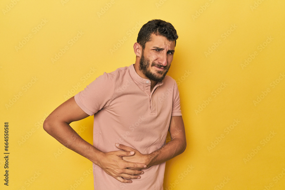 Young Hispanic man on yellow background having a liver pain, stomach ache. Young Hispanic man on yellow background having a liver pain, stomach ache.
