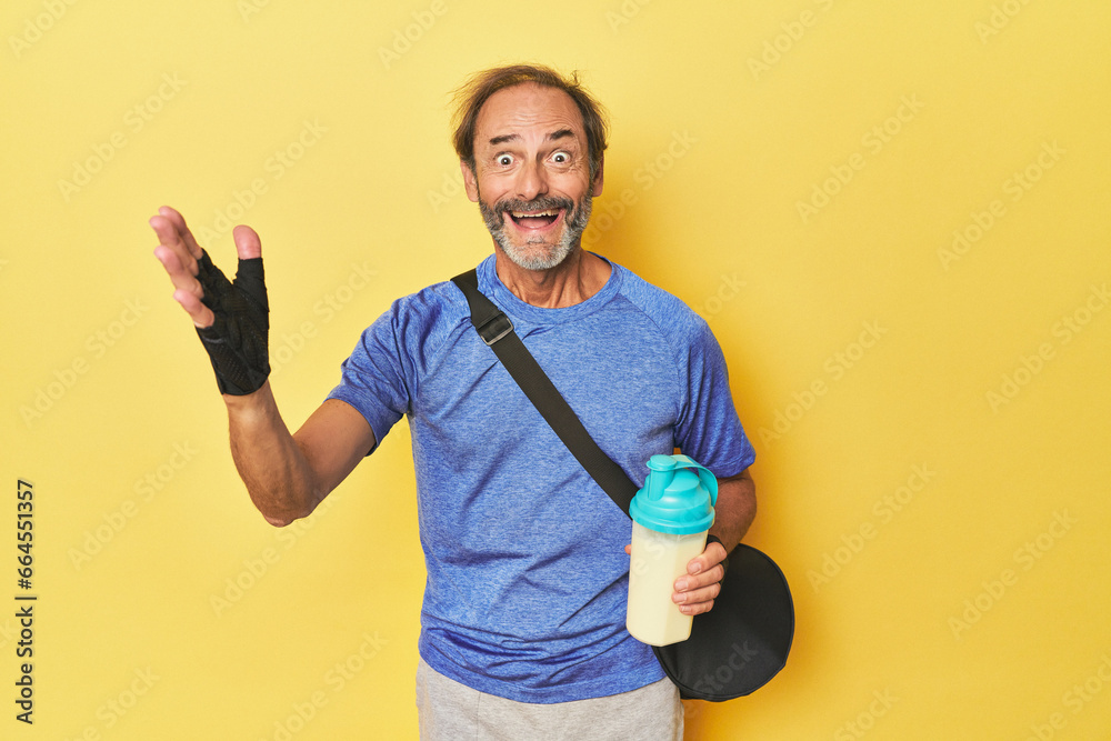 Gym-goer with protein shake in studio receiving a pleasant surprise, excited and raising hands. Gym-goer with protein shake in studio receiving a pleasant surprise, excited and raising hands.