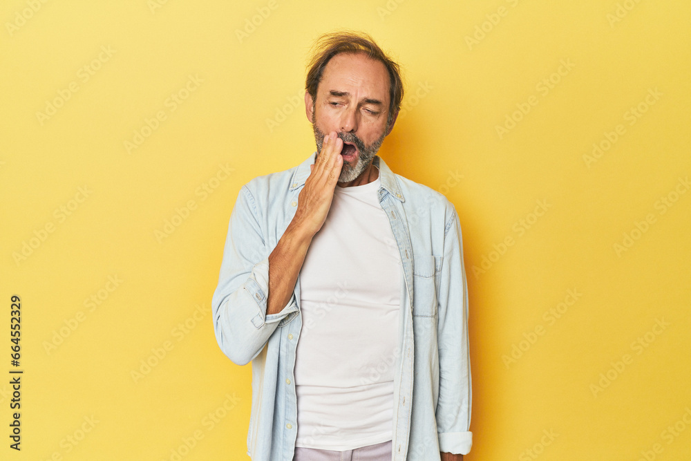 Caucasian middle-aged man in yellow studio yawning showing a tired gesture covering mouth with hand. Caucasian middle-aged man in yellow studio yawning showing a tired gesture covering mouth with hand.