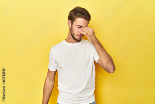Young Caucasian man on a yellow studio background having a head ache, touching front of the face.