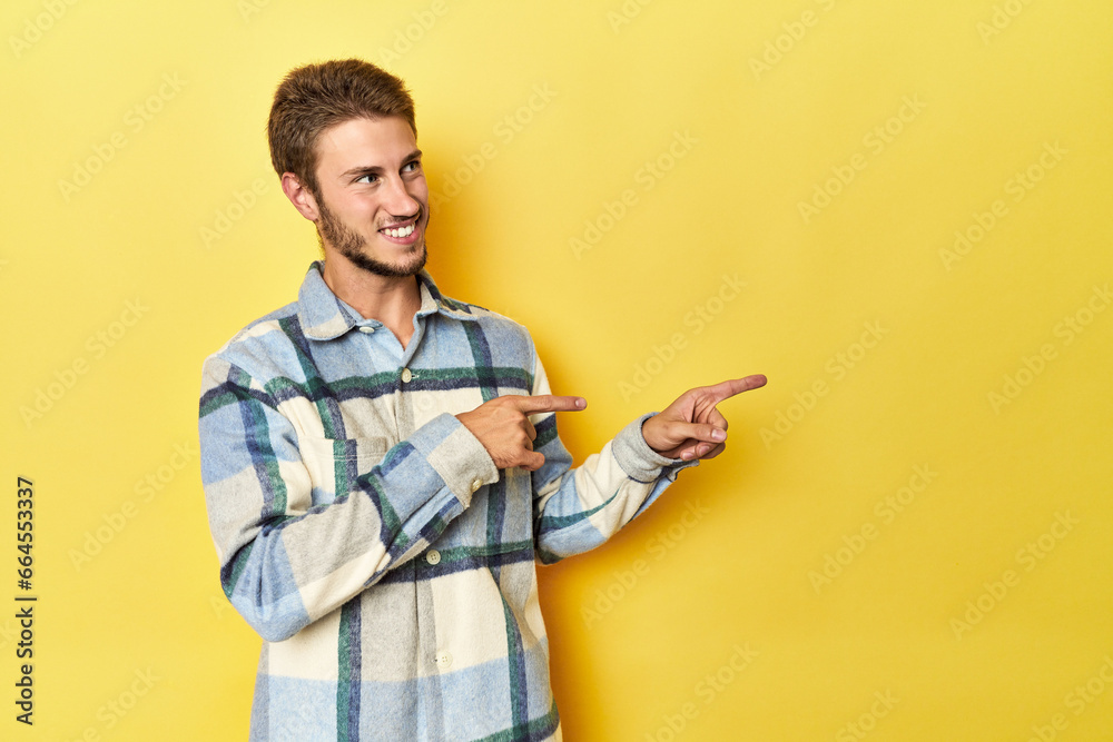 Young Caucasian man on a yellow studio background excited pointing with forefingers away. Young Caucasian man on a yellow studio background excited pointing with forefingers away.