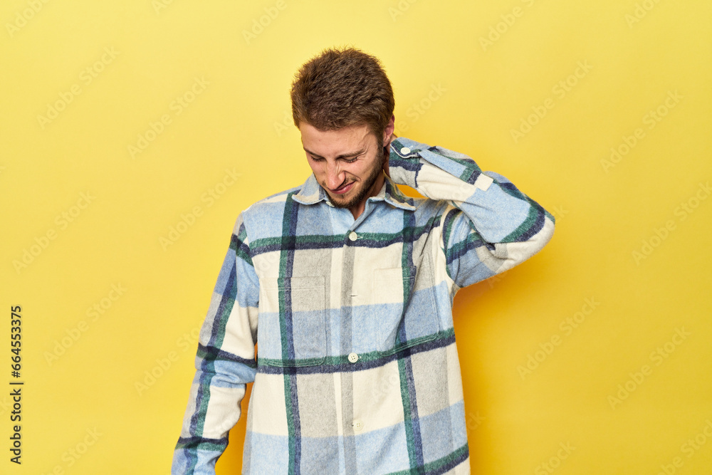 Young Caucasian man on a yellow studio background suffering neck pain due to sedentary lifestyle. Young Caucasian man on a yellow studio background suffering neck pain due to sedentary lifestyle.