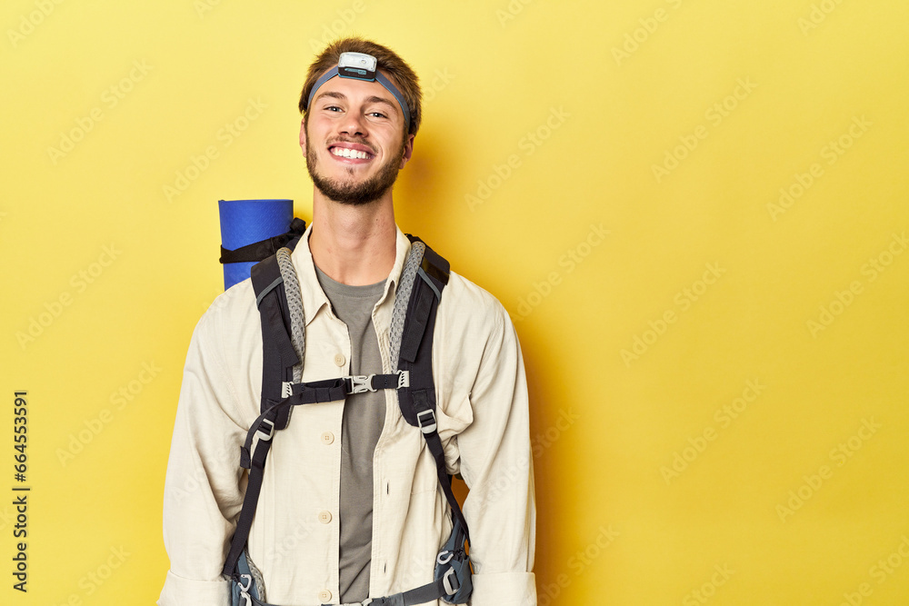 Traveler with mountain backpack, mat, and headlamp on yellow backdrop